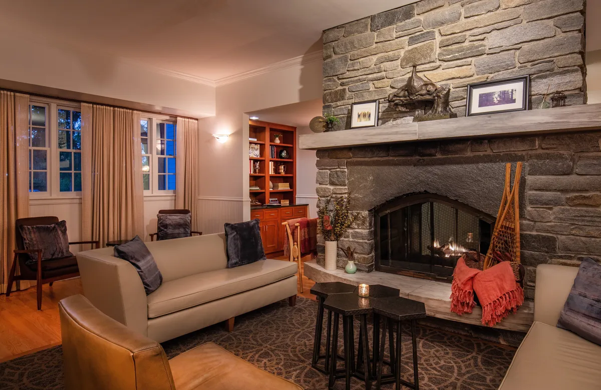 A warm, elegantly appointed lounge area with a stone fireplace flanked by comfortable sofas and decorative items on the mantel. The inviting setting is ideal for unwinding, reading, or enjoying a quiet conversation, echoing the welcoming New England retreat aesthetic.