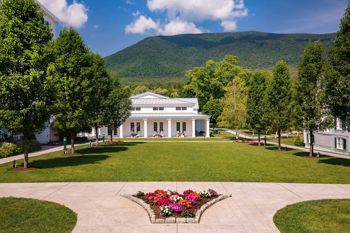 A beautifully landscaped, expansive lawn framed by vibrant flowerbeds and set against a dramatic mountain backdrop, with the iconic white building in view. The scene is serene, inviting, and perfectly suited for outdoor gatherings, picnics, or strolls with pets.