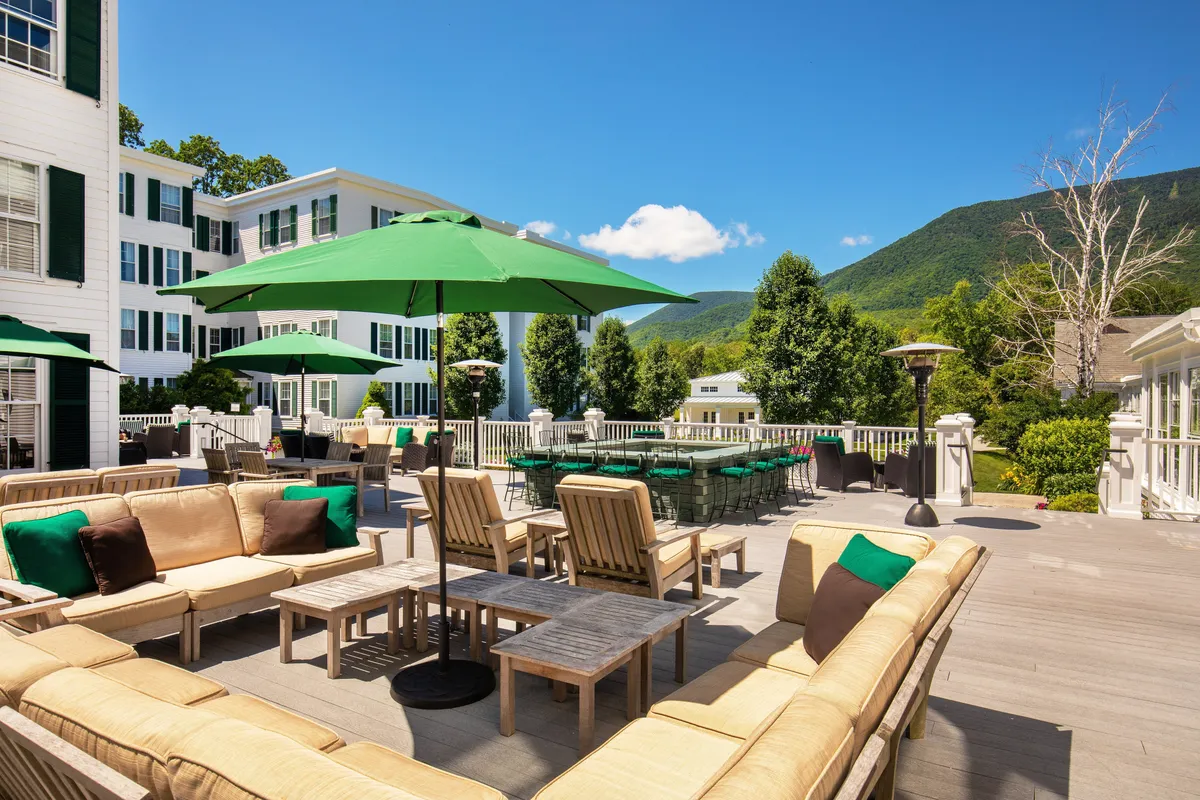 A spacious outdoor seating area with green umbrellas, comfortable chairs, and a panoramic view of the mountains. The scene invites leisurely moments of relaxation, social gatherings, or soaking in the natural beauty of the resort's surroundings.